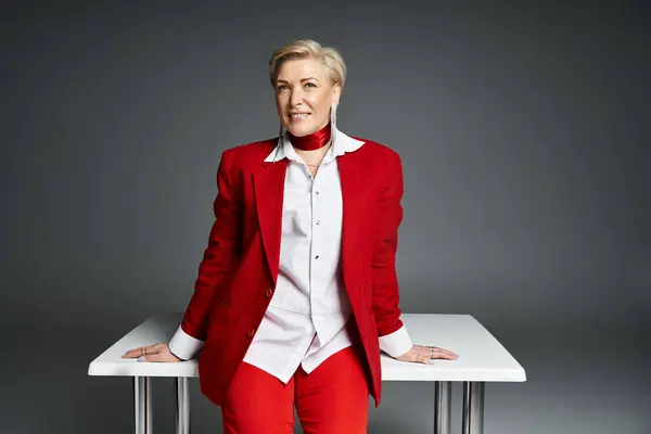 A confident woman in a chic red outfit strikes a stylish pose at a sleek table. — Stock Photo