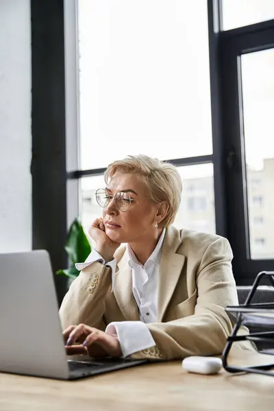 A sophisticated woman in elegant attire contemplates while working on her laptop during daylight. — Stock Photo
