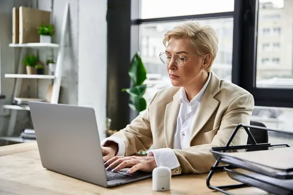 An elegant woman diligently types on her laptop, surrounded by a contemporary workspace. — Stock Photo