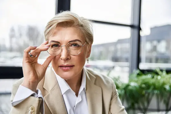 Eine erwachsene Frau in eleganter Kleidung blickt nachdenklich durch ihre Brille und strahlt Zuversicht aus.. — Stockfoto