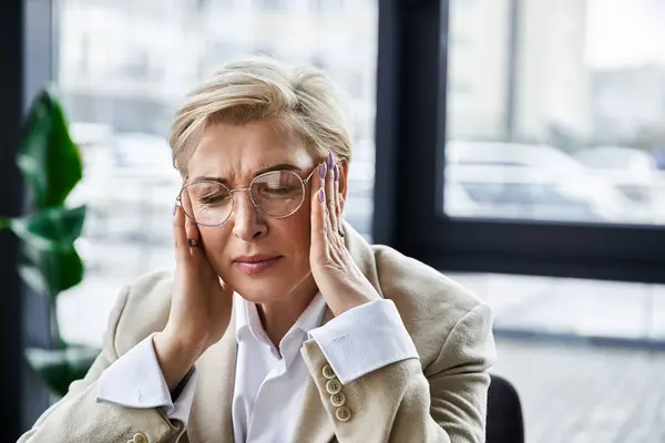 A fashionable adult woman shows signs of frustration while at her desk in an office setting. — Stock Photo
