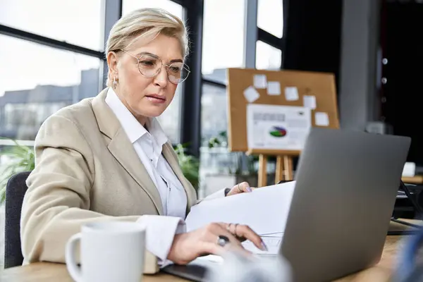 Uma mulher adulta vestida elegantemente se envolve com seu laptop em uma mesa de escritório contemporânea. — Fotografia de Stock