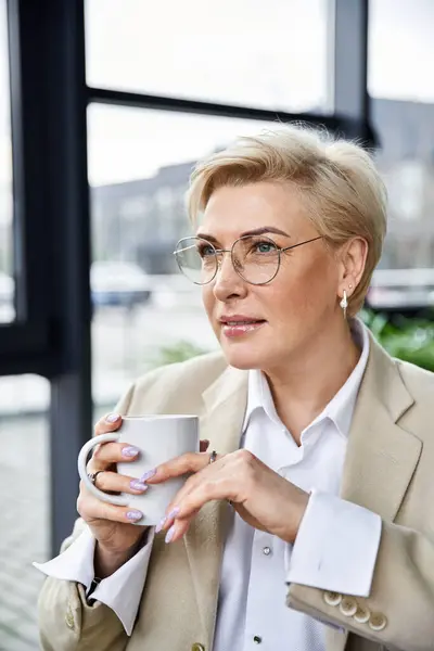 Eine kultivierte Frau nippt nachdenklich an ihrem Kaffee, elegant gekleidet, während sie sich entspannt. — Stockfoto