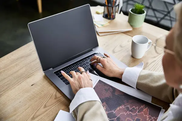 Una mujer adulta elegante se centra en su portátil mientras disfruta de sus vibraciones de espacio de trabajo con café. - foto de stock