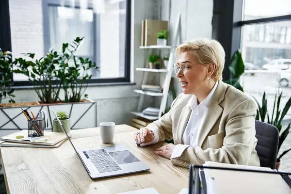 Una donna adulta in abiti alla moda partecipa a una discussione virtuale presso una scrivania ben illuminata. — Foto stock