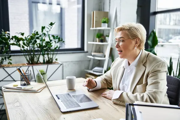 An elegantly dressed woman converses intently while seated at her stylish office desk. — Stock Photo