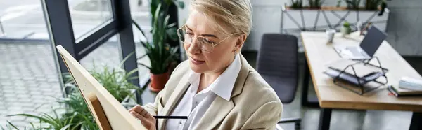 A stylish adult woman focuses intently on her easel, surrounded by plants and natural light. — Stock Photo
