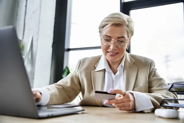 An adult stylish woman in elegant attire browses online shopping while seated at her desk. — Stock Photo