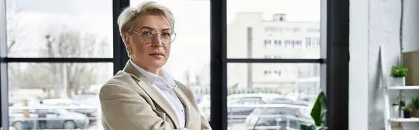Una mujer confiada vestida con un atuendo elegante se encuentra en una oficina contemporánea, exudando estilo. - foto de stock