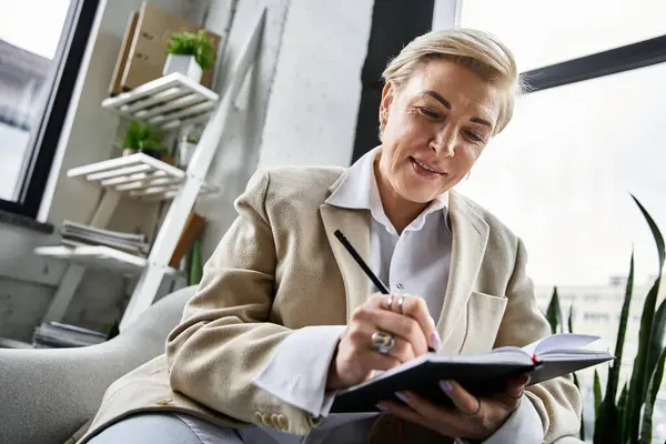 A sophisticated woman writes intently in a notebook while surrounded by plants and natural light. — Stock Photo