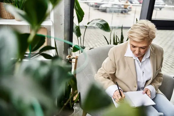 An adult woman dressed elegantly sits thoughtfully, jotting down ideas in her notebook. — Stock Photo