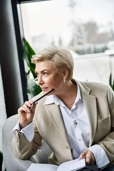 An adult woman in sophisticated clothing contemplates while sitting in a chic office setting. — Stock Photo