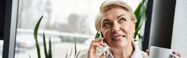 An elegant woman chats on the phone with a charming smile, sipping her drink amidst greenery. — Stock Photo