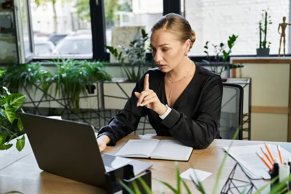 A young plus size woman focuses intently on her laptop, surrounded by plants and notes. — Stock Photo