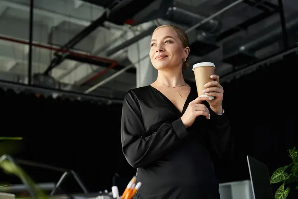 Женщина plus size уверенно стоит в офисе, потягивая кофе, пока она концентрируется на своих задачах. — стоковое фото
