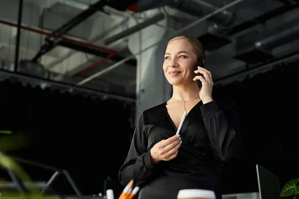 The young woman enjoys a phone conversation while working diligently at her desk. — Stock Photo