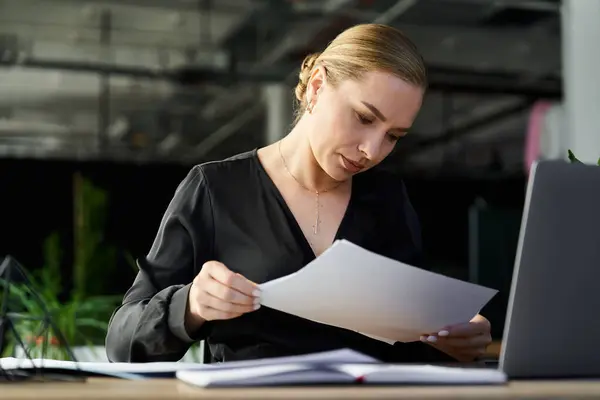 A focused young woman examines paperwork while seated at her office desk, showcasing determination. — Stock Photo