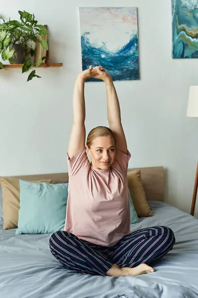 A young plus size woman relaxes by stretching her arms in a stylish bedroom filled with art. — Stock Photo