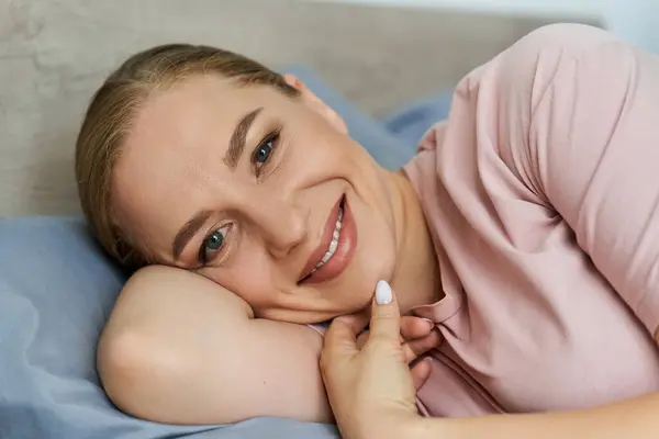 A young woman relaxes comfortably at home, smiling brightly while lying on soft bedding. — Stock Photo