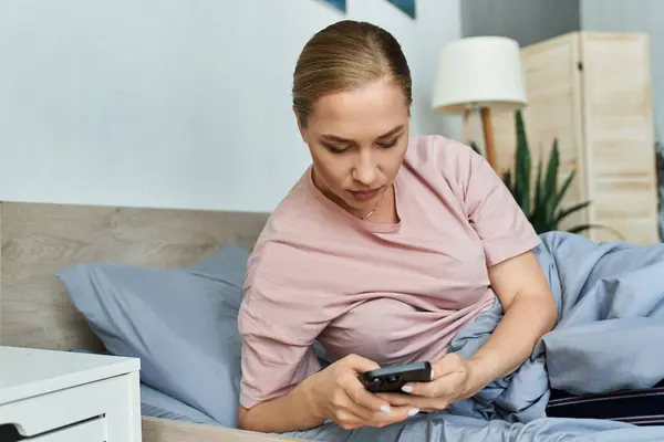 A young woman lounges comfortably in bed, engaged with her smartphone, embracing a cozy morning. — Stock Photo