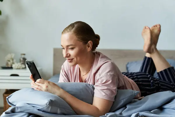 A young woman lounges comfortably on her bed, engaged with her phone, smiling warmly. — Stock Photo