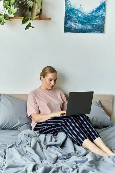 A young beautiful plus size woman sits comfortably on her bed, focused on her laptop. — Stock Photo