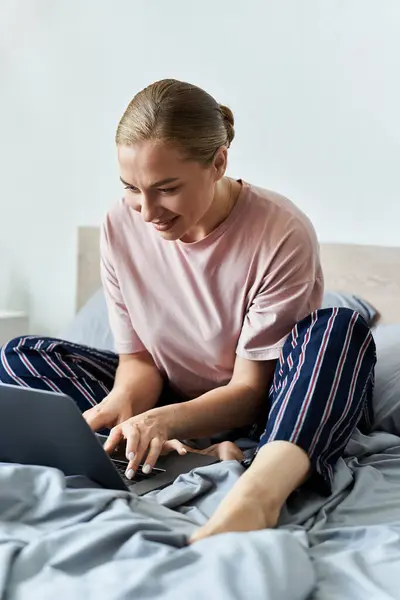 A cheerful plus size woman sits cross legged on her bed, focused on her laptop in a serene space. — Stock Photo