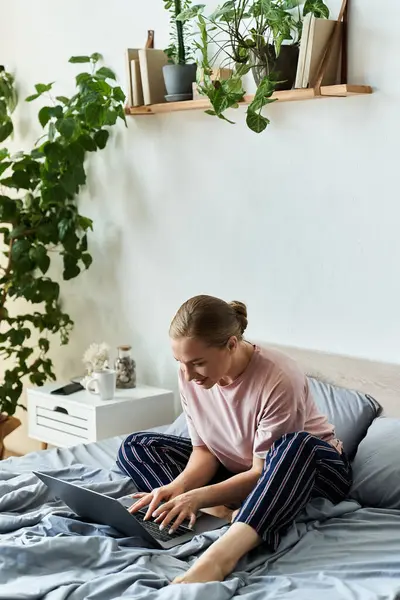 A young woman relaxes on her bed, typing on a laptop in a stylish home environment. — Stock Photo