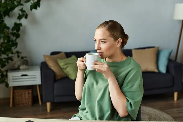 A young woman relaxes at home, sipping from a cozy mug while enjoying her space. — Stock Photo