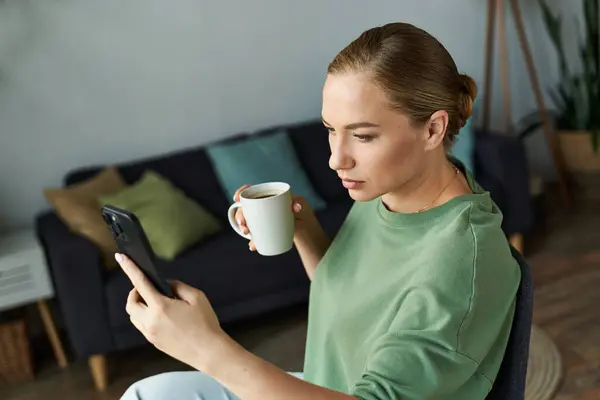 A beautiful plus size woman relaxes at home, sipping coffee and checking her phone with focus. — Stock Photo