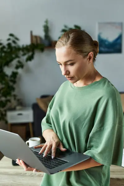 La giovane donna si concentra sul suo computer portatile mentre circondata da un ambiente domestico caldo e invitante. — Foto stock