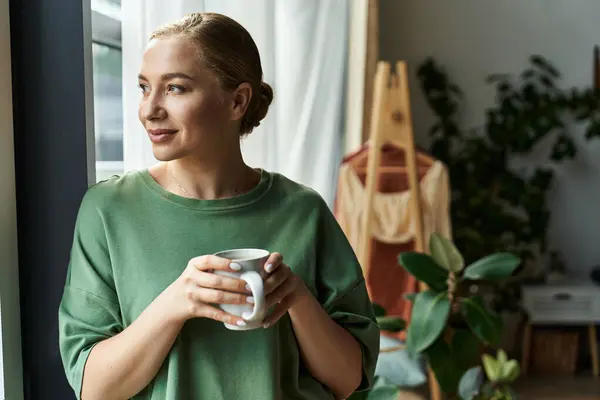 A young woman relaxes at home, thoughtfully sipping tea by the window with a cozy ambiance. — Stock Photo