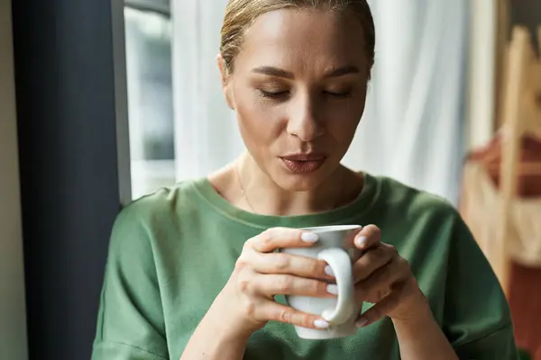 Una giovane donna assapora il suo ambiente domestico accogliente mentre tiene in mano una tazza calda, rilassandosi in tranquillità. — Foto stock