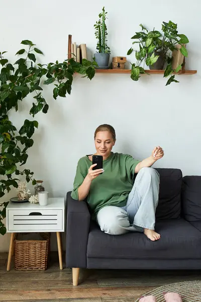 Eine fröhliche Plus-Size-Frau entspannt sich auf ihrer Couch und scrollt in einem friedlichen Raum auf ihrem Smartphone. — Stockfoto