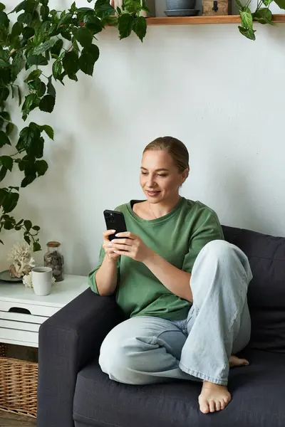 A cheerful plus size woman enjoys her time at home, comfortably texting on her smartphone. — Stock Photo