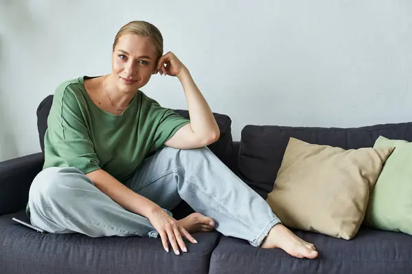 A cheerful young woman with a graceful pose enjoys a moment of tranquility on her sofa. — Stock Photo