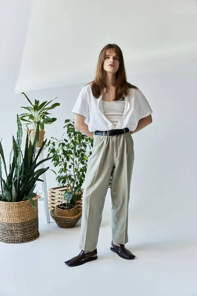 A young person showcases their trendy outfit amidst vibrant indoor plants in a modern space. — Stock Photo