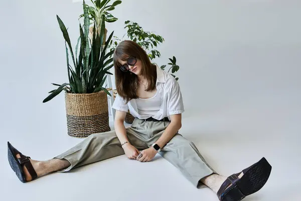 Um jovem moderno posa confortavelmente no chão, cercado por plantas envasadas exuberantes. — Fotografia de Stock