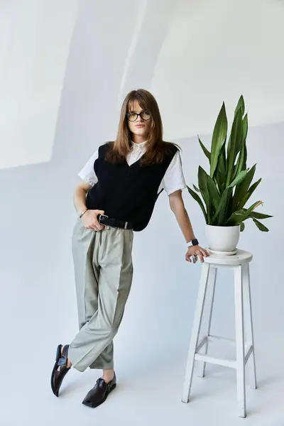 A young man dressed in fashionable attire leans against a plant stand, showcasing his unique style. — Stock Photo