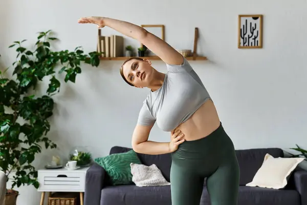A young sportive woman in stylish active wear engages in a home workout, stretching gracefully. — Stock Photo
