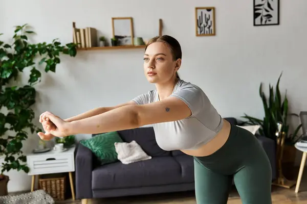 Uma jovem mulher em um top de cultura e leggings se concentra em seu treino em casa, mostrando força e determinação. — Fotografia de Stock