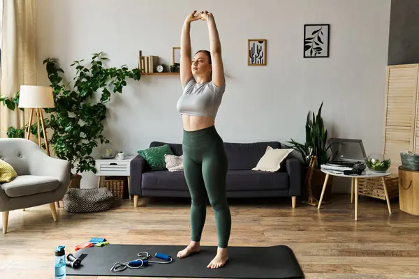 A sportive woman stretches her arms high while exercising at home in chic fitness apparel. — Stock Photo