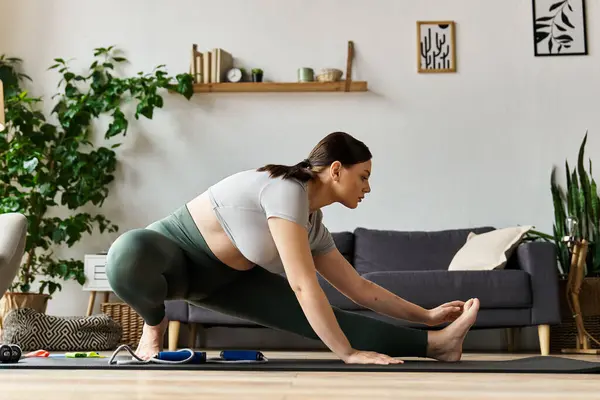 A young sportive woman stretches in her crop top and leggings during an energizing home workout session. — Stock Photo