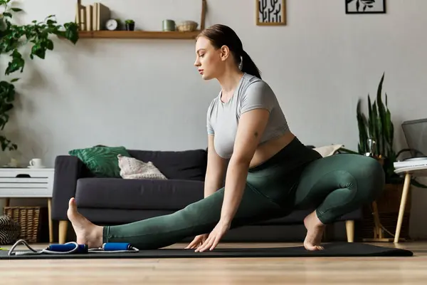 A young sportive woman focuses on her flexibility while exercising at home in stylish active wear. — Stock Photo