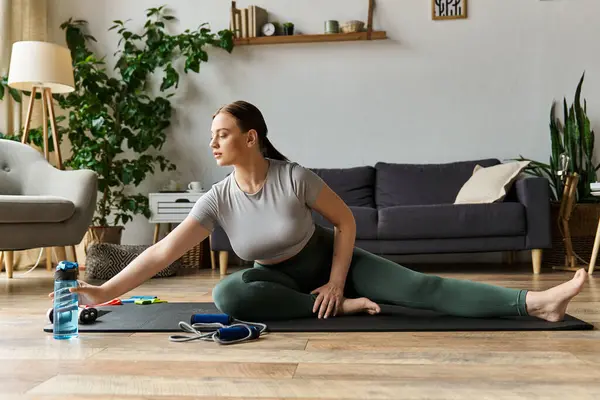 A sportive woman stretches on a mat during her home workout routine, showcasing her dedication and focus. — Stock Photo