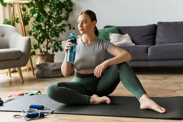 Une jeune femme sportive prend une pause pour s'hydrater après un entraînement énergique à la maison, se sentant accomplie. — Photo de stock