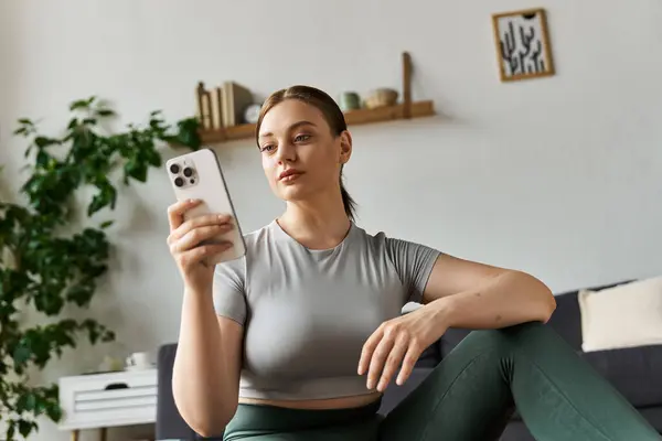 A young sportive woman in active wear focuses on her phone during a home workout session. — Stock Photo