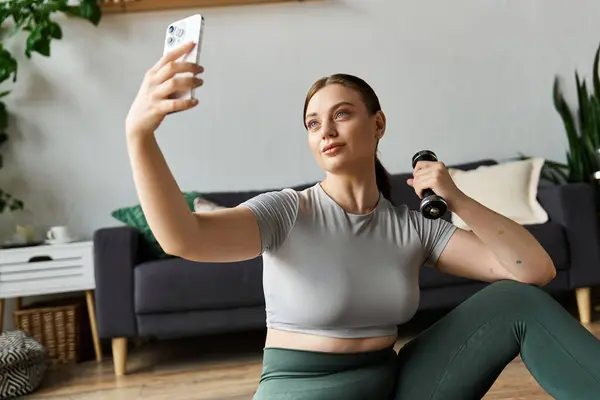 Una donna sportiva in crop top e leggings si impegna in un allenamento a casa mentre prende un selfie. — Foto stock