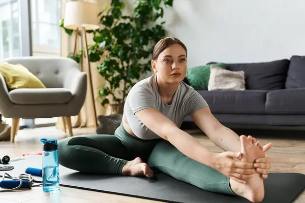 Спортивная молодая женщина в модной спортивной одежде выполняет глубокую растяжку на своем коврике для йоги дома. — стоковое фото