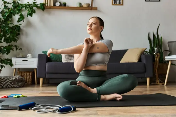 Sportive woman practices a stretching routine in stylish active wear on her living room floor. — Stock Photo